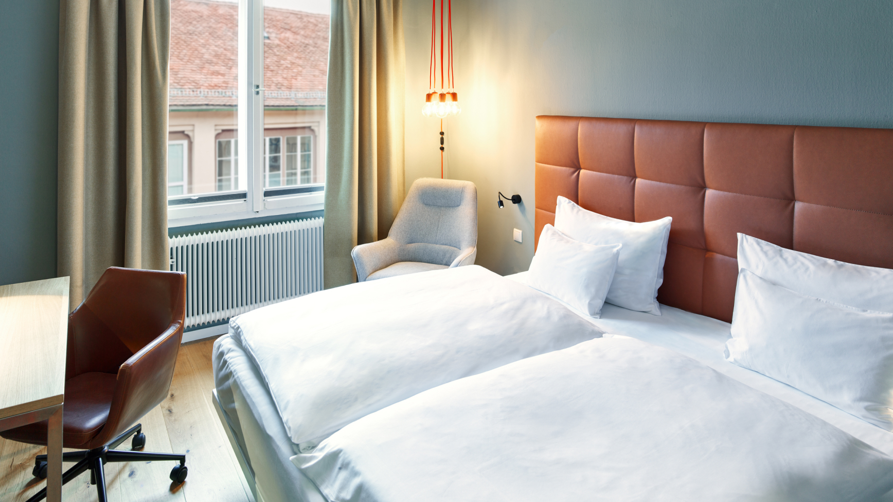 Ein Hotelzimmer mit zwei Betten, einem Schreibtisch, einem Sessel und einem Fenster.