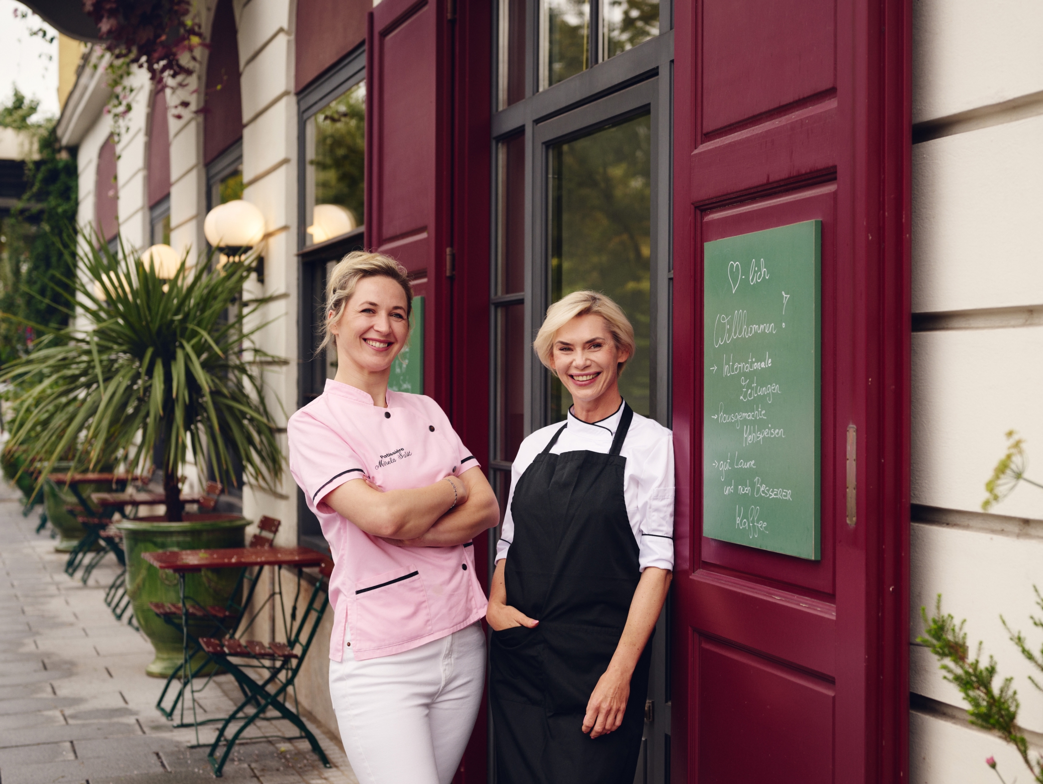 Zwei Köche stehen vor "Restaurant Mirabella" mit einer Tafel, die "Willkommen!" sagt.