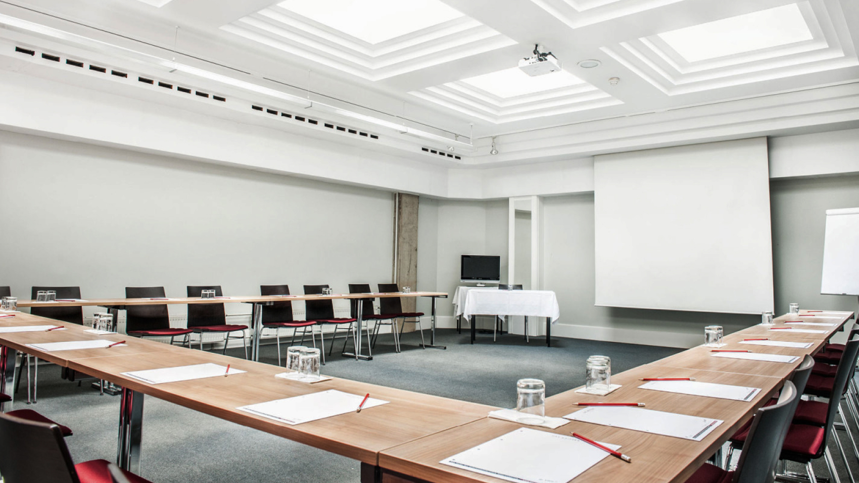 Konferenzraum mit U-förmiger Tischordnung, Projektor, Leinwand und Flipchart.