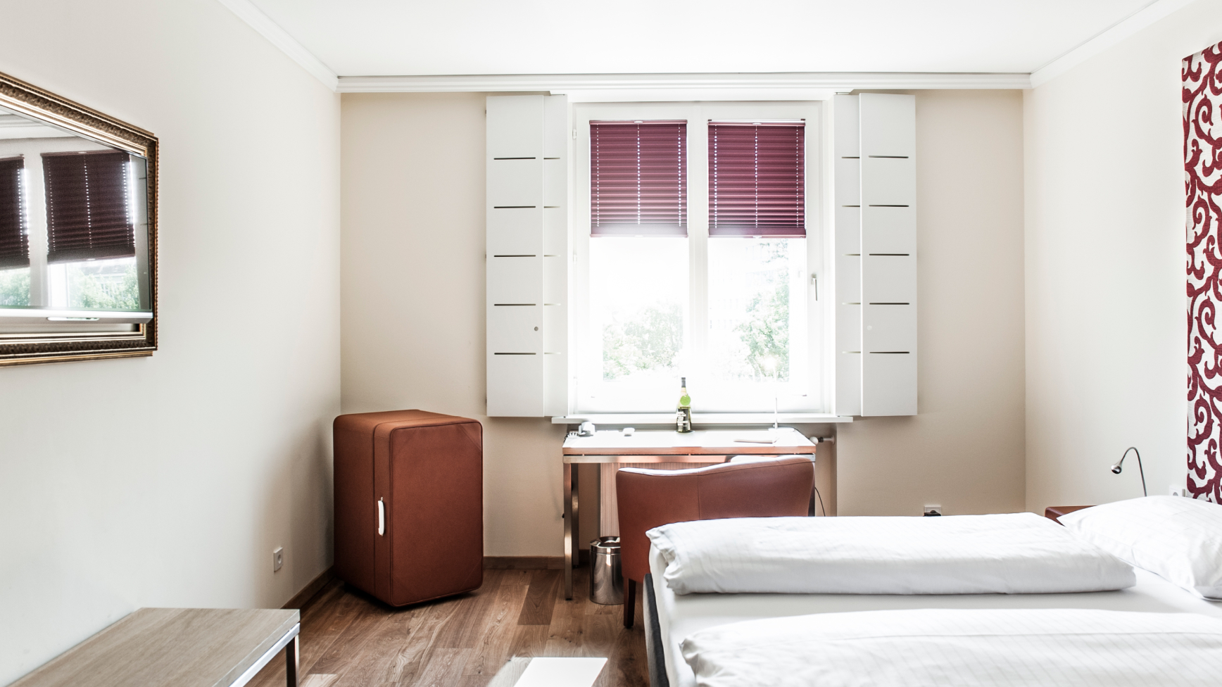 Innenaufnahme eines Hotelzimmers mit Bett, Schreibtisch am Fenster und einem braunen Schrank.