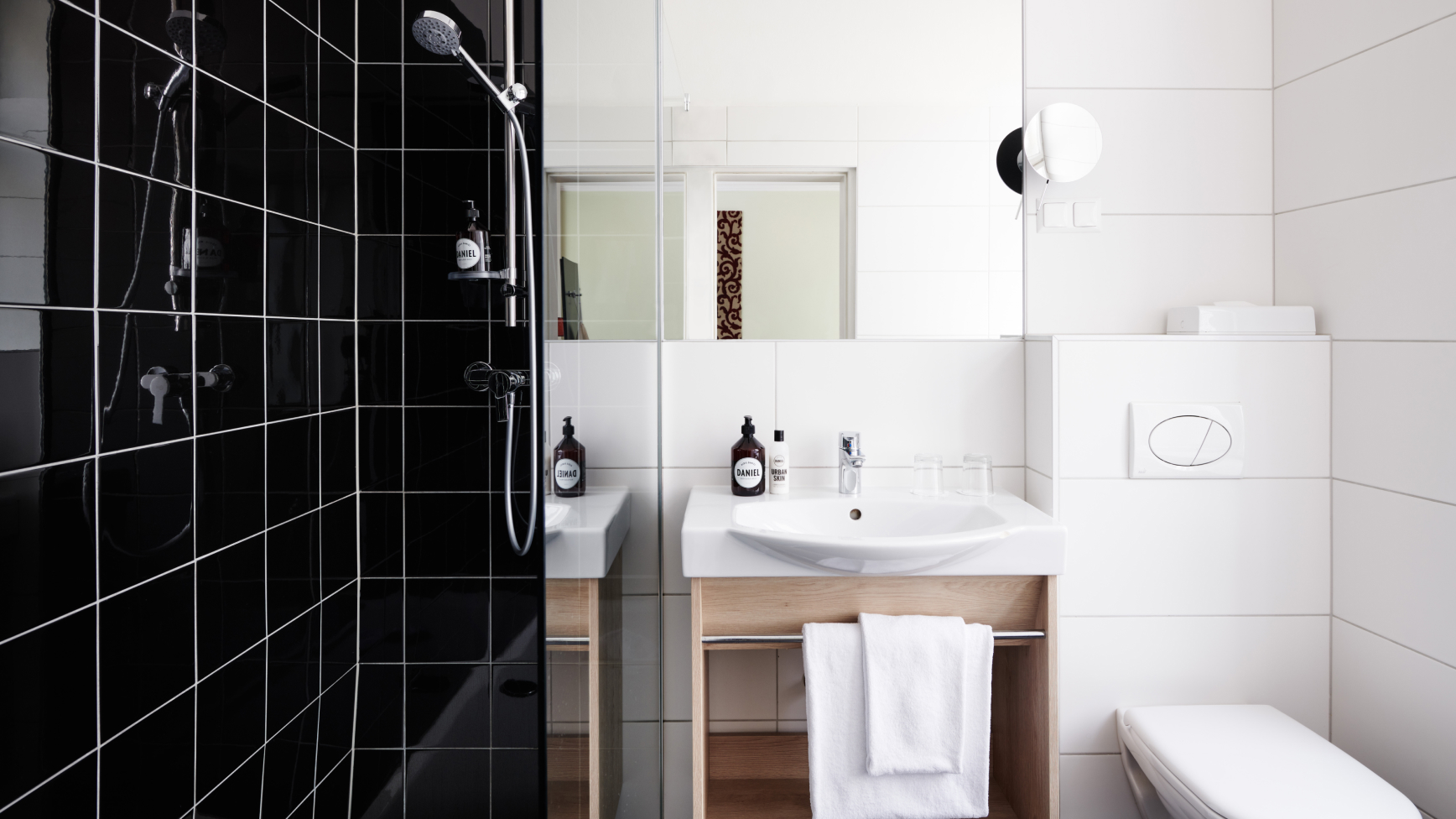 Modernes Badezimmer mit schwarzer gefliester Dusche, Waschbecken, Spiegel und Toilette. Handtücher hängen unter dem Waschbecken.