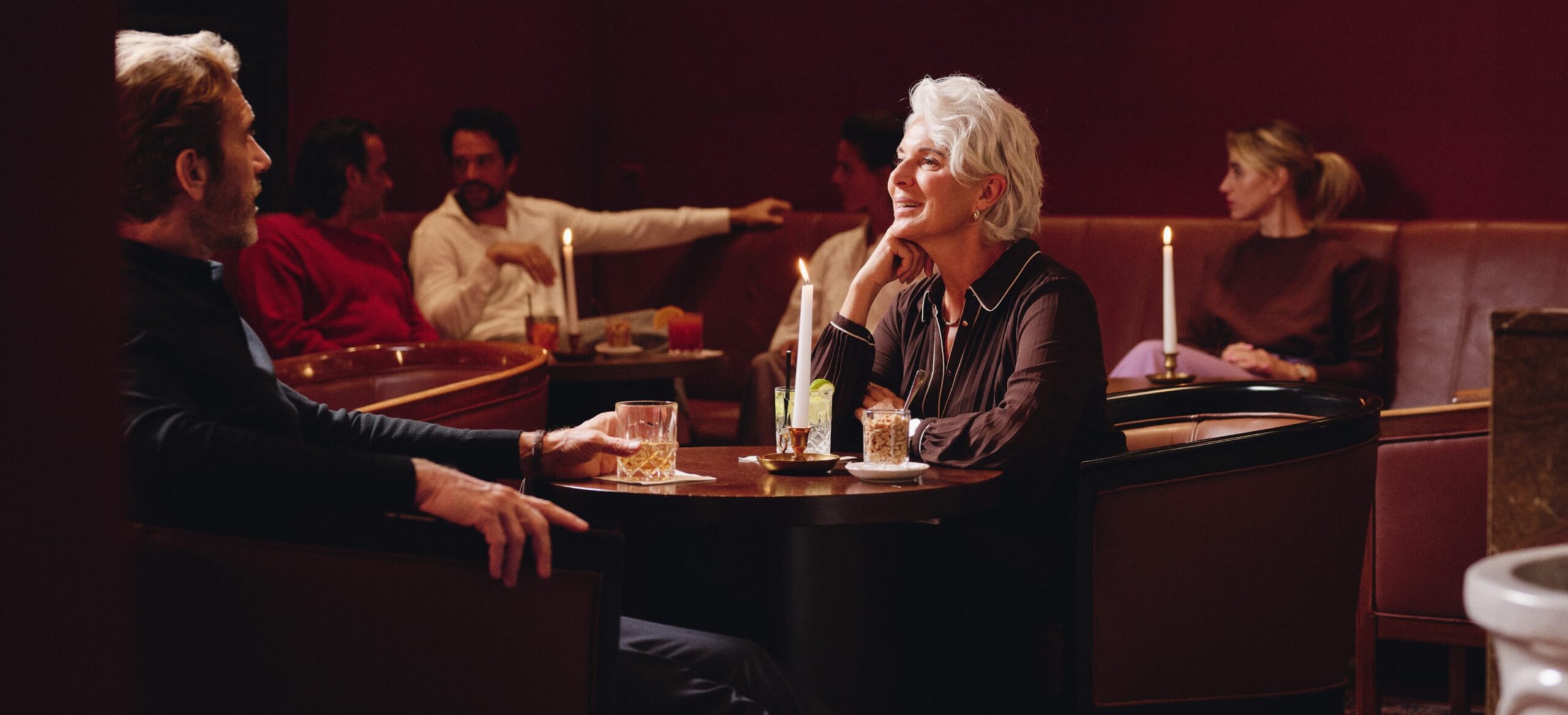 Innenaufnahme eines dunklen Bars mit mehreren Personen, die an Tischen sitzen und Getränke genießen.