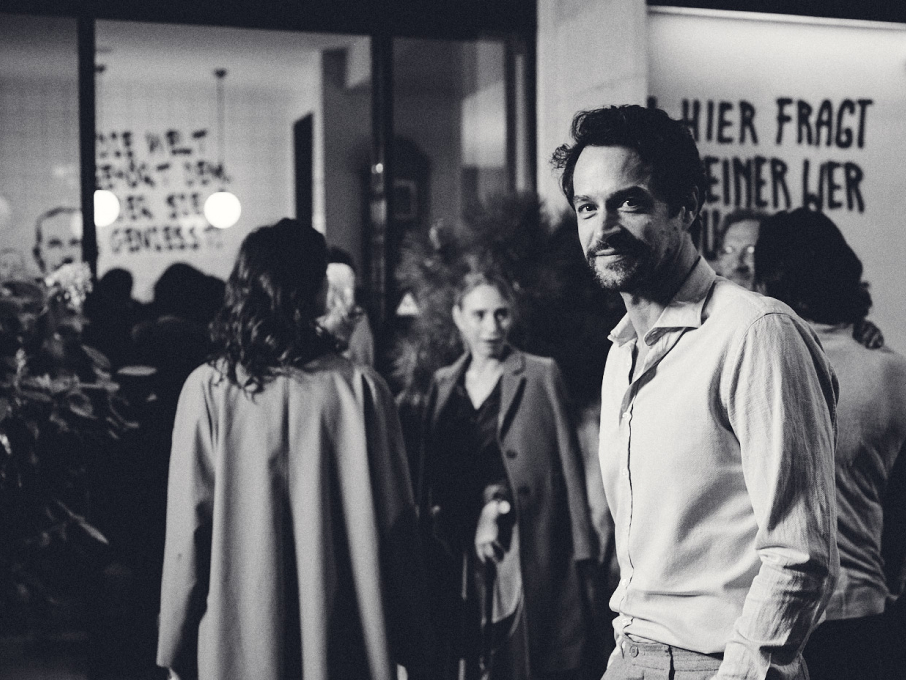 Schwarzweißfoto eines Mannes im Hemd vor einer belebten Straßenszene mit Graffiti.