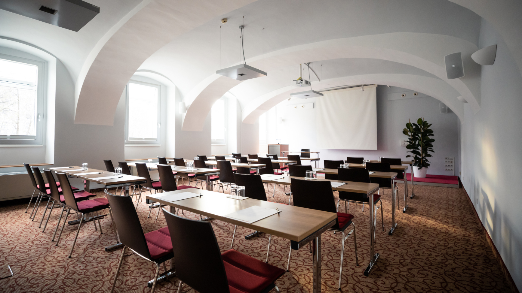 Ein hell erleuchteter Konferenzraum mit Tischen, Stühlen und Projektor unter einer gewölbten Decke.