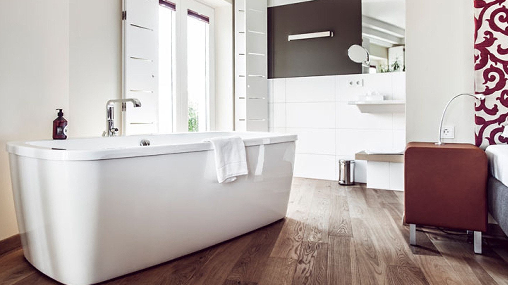 Ein Badezimmer mit einer weißen Badewanne, Holzfußboden und einem Fenster mit Fensterläden.