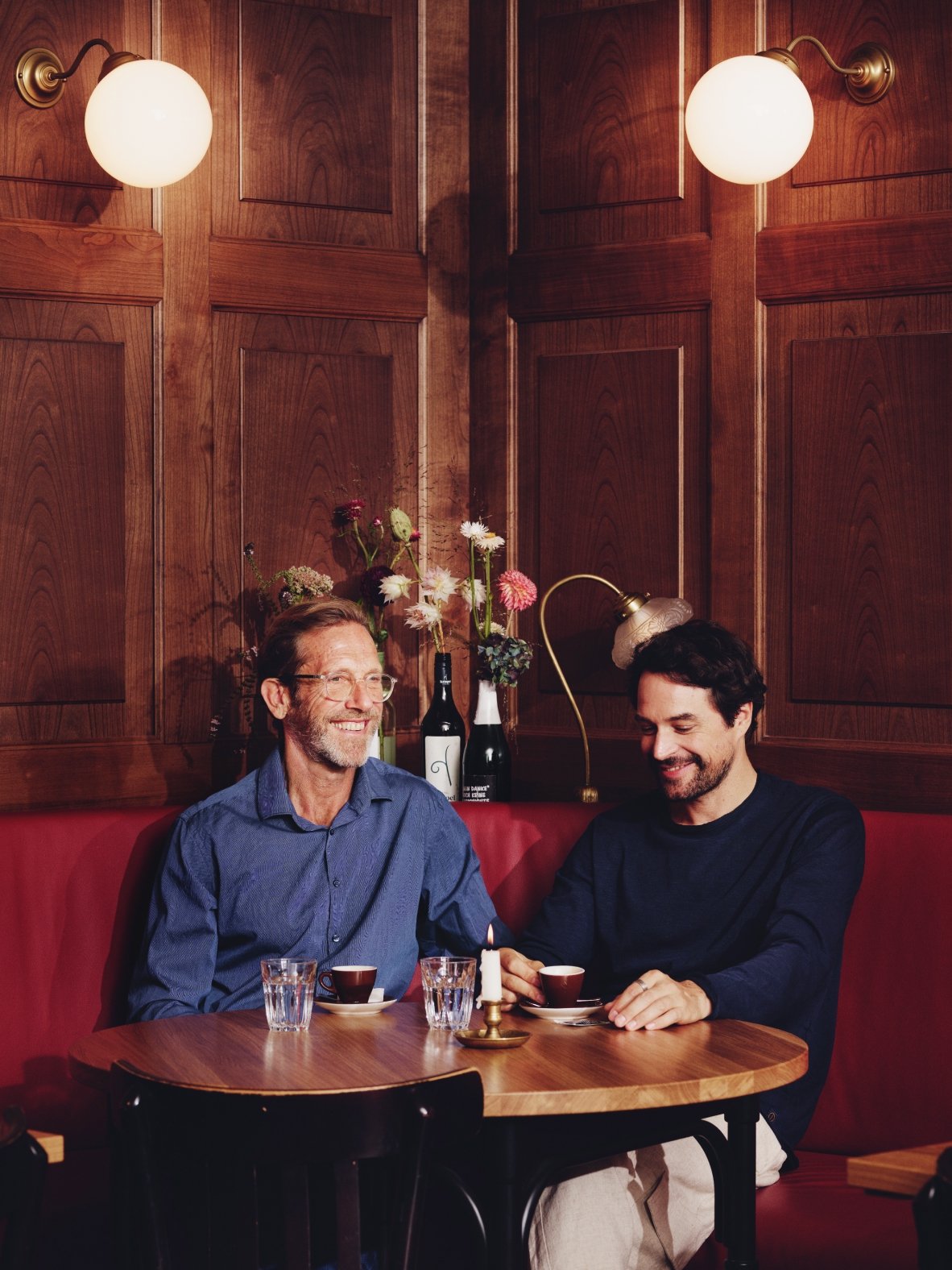 Zwei Männer sitzen an einem Tisch in einem holzgetäfelten Restaurant mit roten Sitzen.