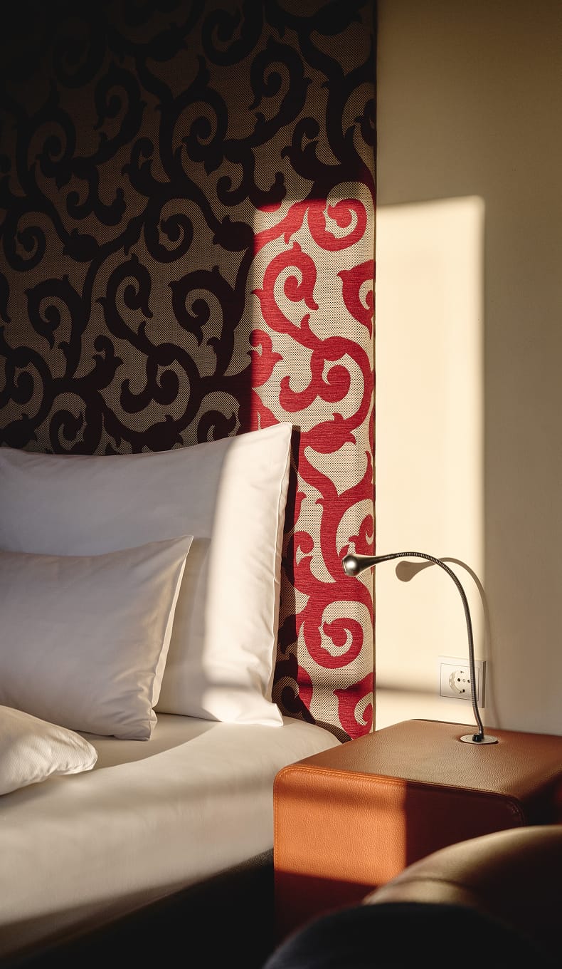 Nahaufnahme von Kissen, Nachttischlampe und kopfteil mit rotem und braunem Wirbelmuster.