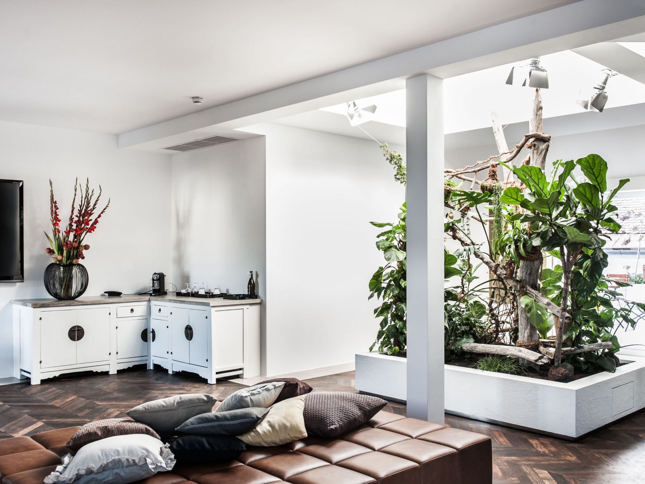 Ein helles Interieur mit braunem Ledersofa, Zierkissen und weißen Schränken. Eine Pflanze steht im Hintergrund.