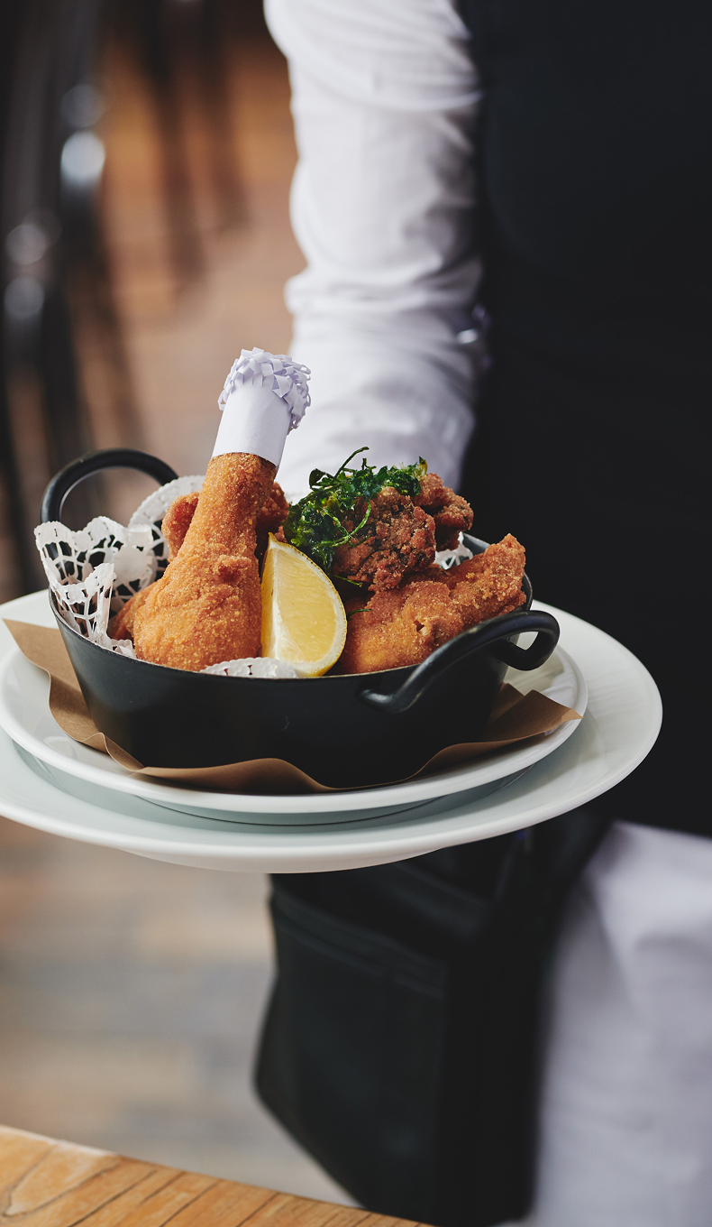 Kellner hält Schüssel mit gebratenem Huhn, einer Zitrone und einem kleinen Kochhut auf einem Teller.