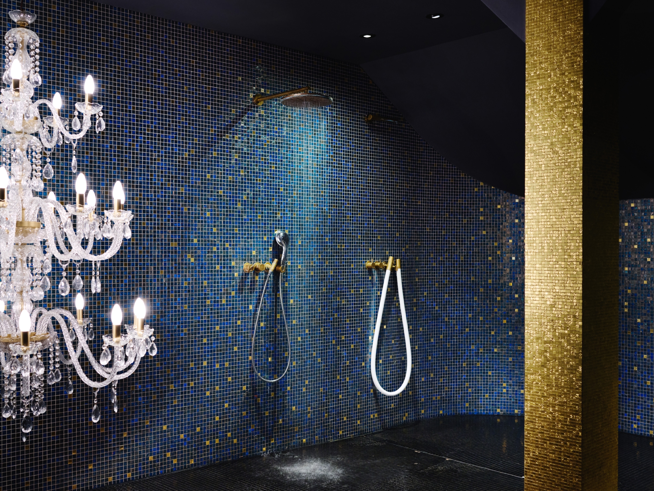 Ein Badezimmer mit blau gefliesten Wänden, einem goldenen Mosaikpfeiler und einem Kronleuchter.