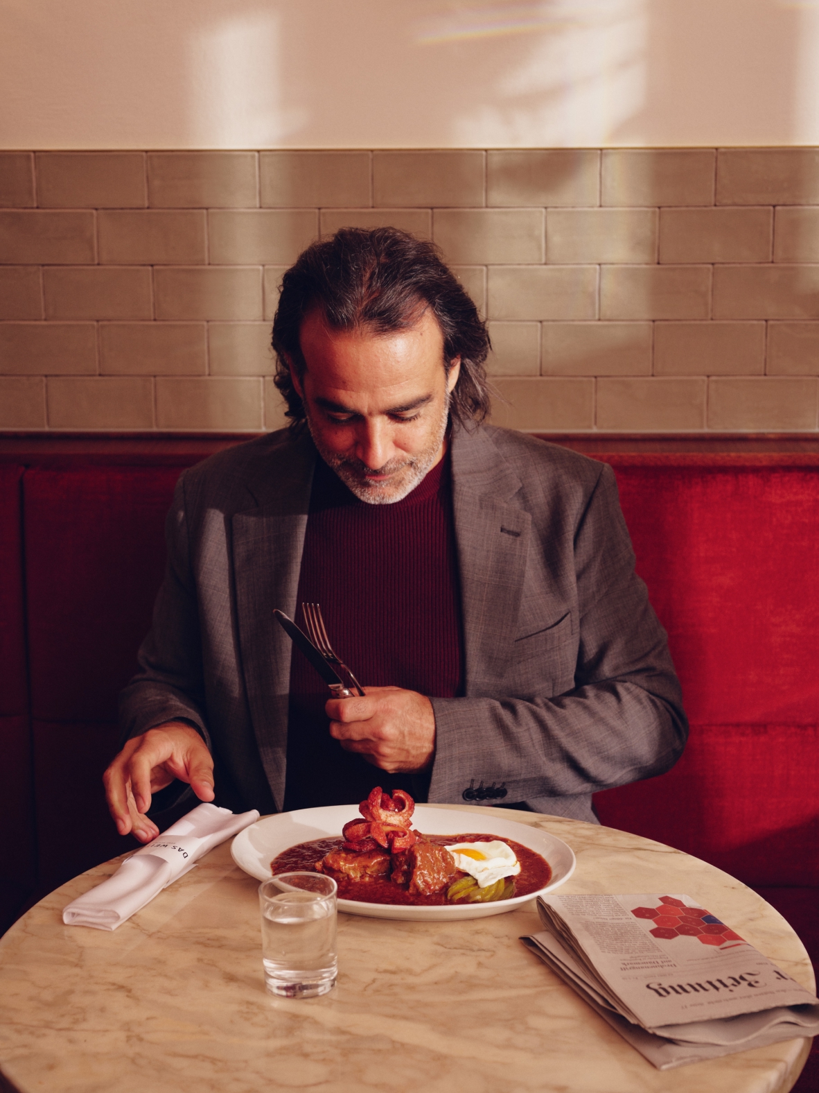 Ein Mann isst einen Fleischgang mit Ei und Zeitung auf dem Tisch.