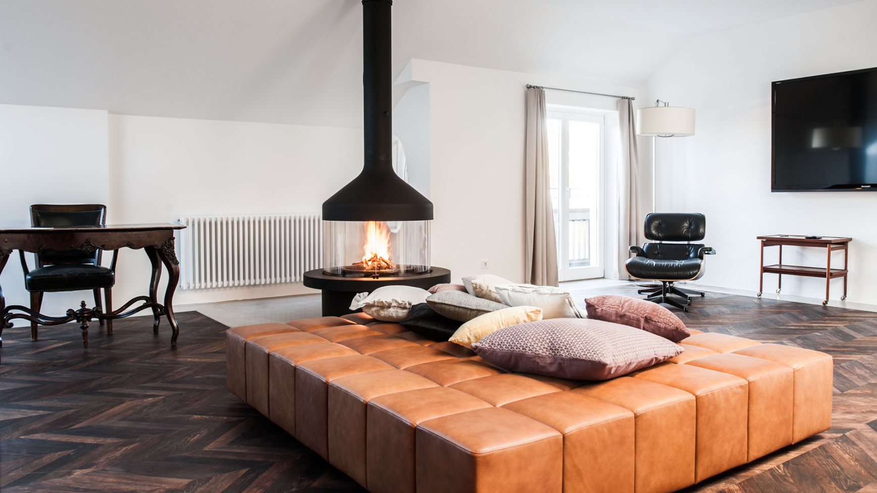 Wohnzimmer mit Ledersofa, Kamin, Schreibtisch, Sessel und Parkettboden.