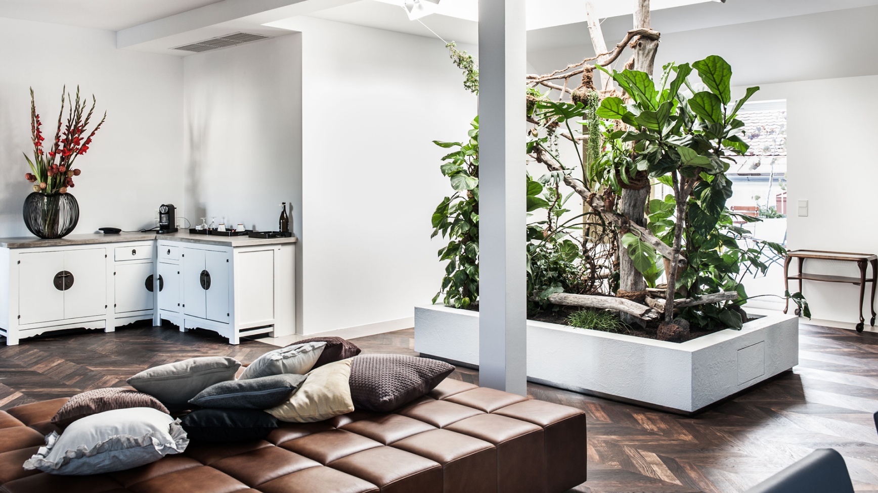 Ein Wohnzimmer mit braunen Ledersitzkissen, weißen Schränken und Innengarten mit Grünpflanzen.