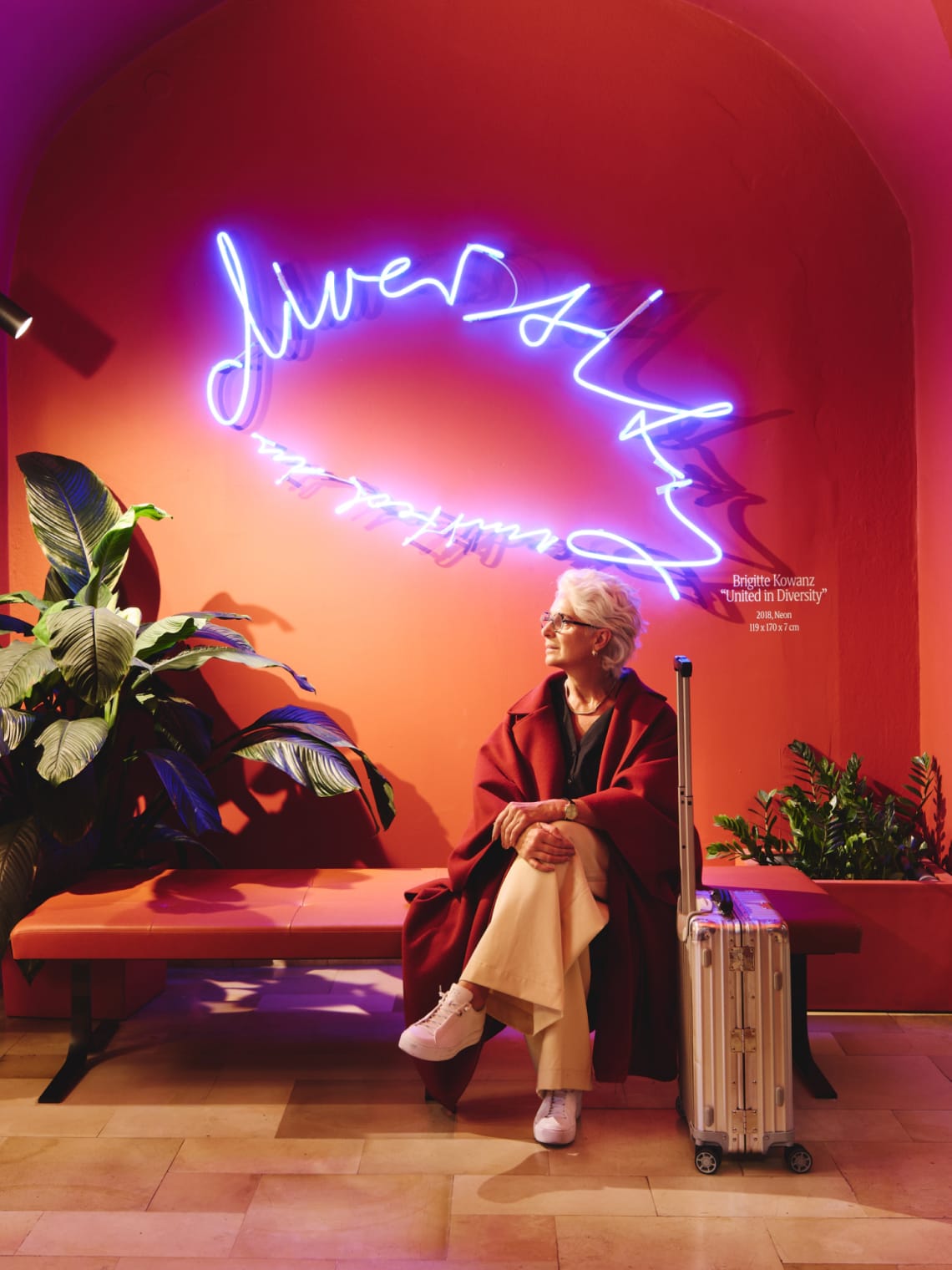 Brigitte Kowanz sitzt auf einer Bank unter einer Neonarbeit mit dem Titel "United in Diversity".