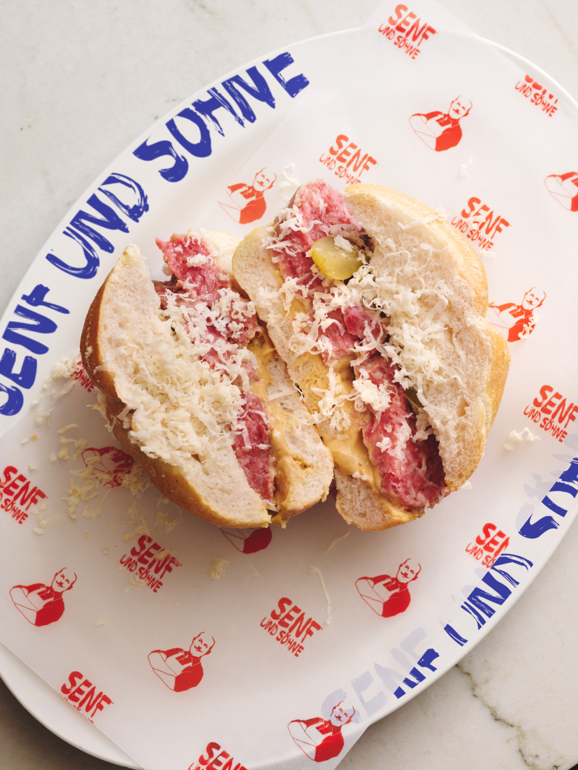 Nahaufnahme von zwei Hälften eines Senf und Söhne-Sandwiches, auf einem Teller mit dem gleichen Aufdruck.
