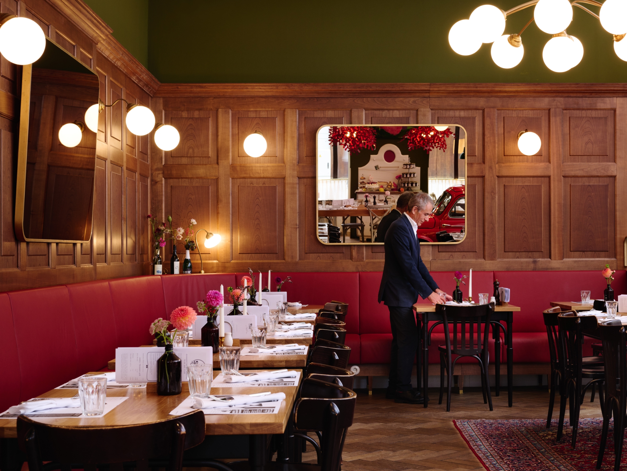 Innenraum eines Restaurants mit Holzvertäfelung, roter Sitzbank, Tischen und einem Mann.