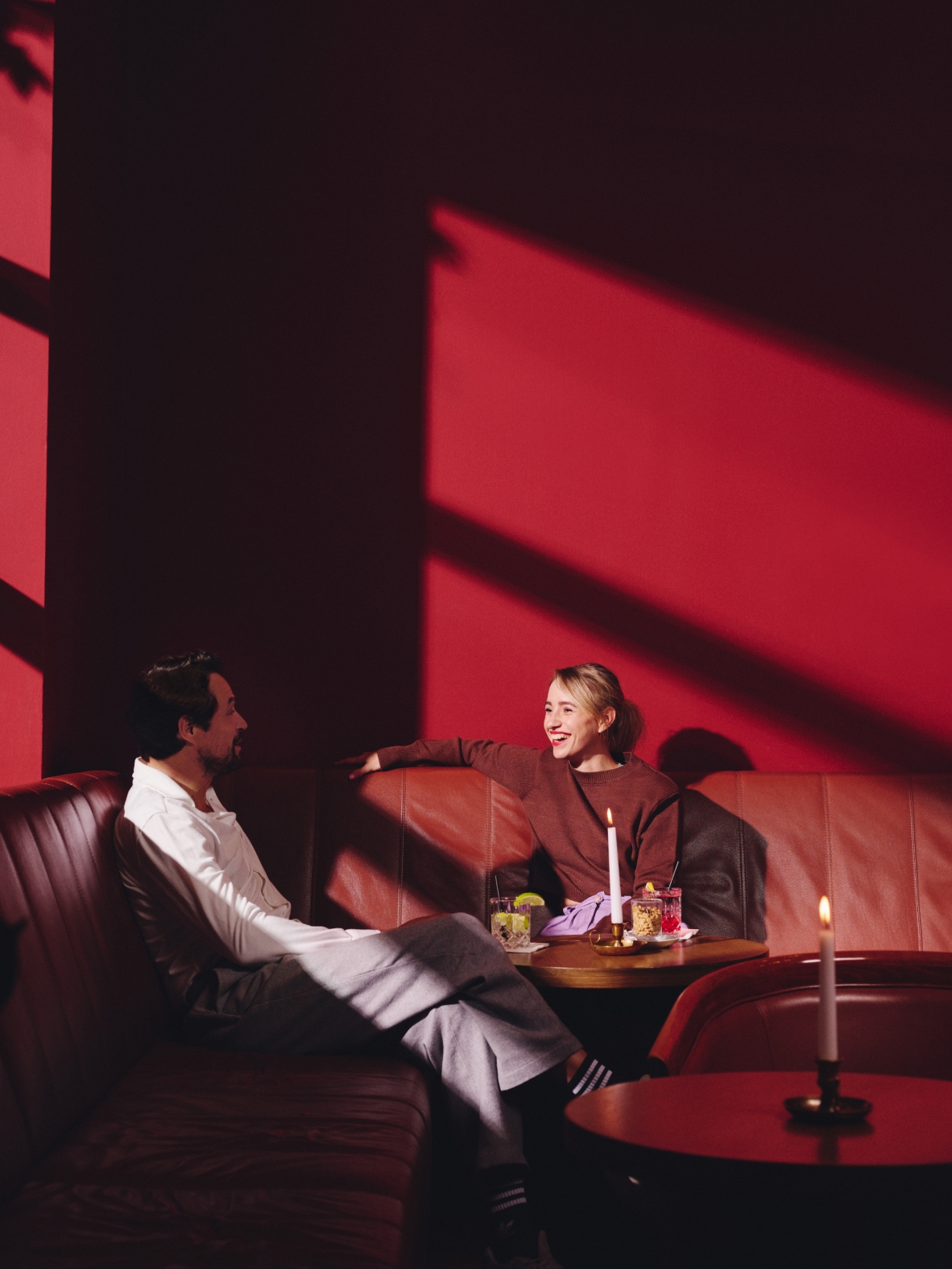 Mann und Frau in einer roten Bar mit Cocktails, Kerzen und einem Ledersofa.