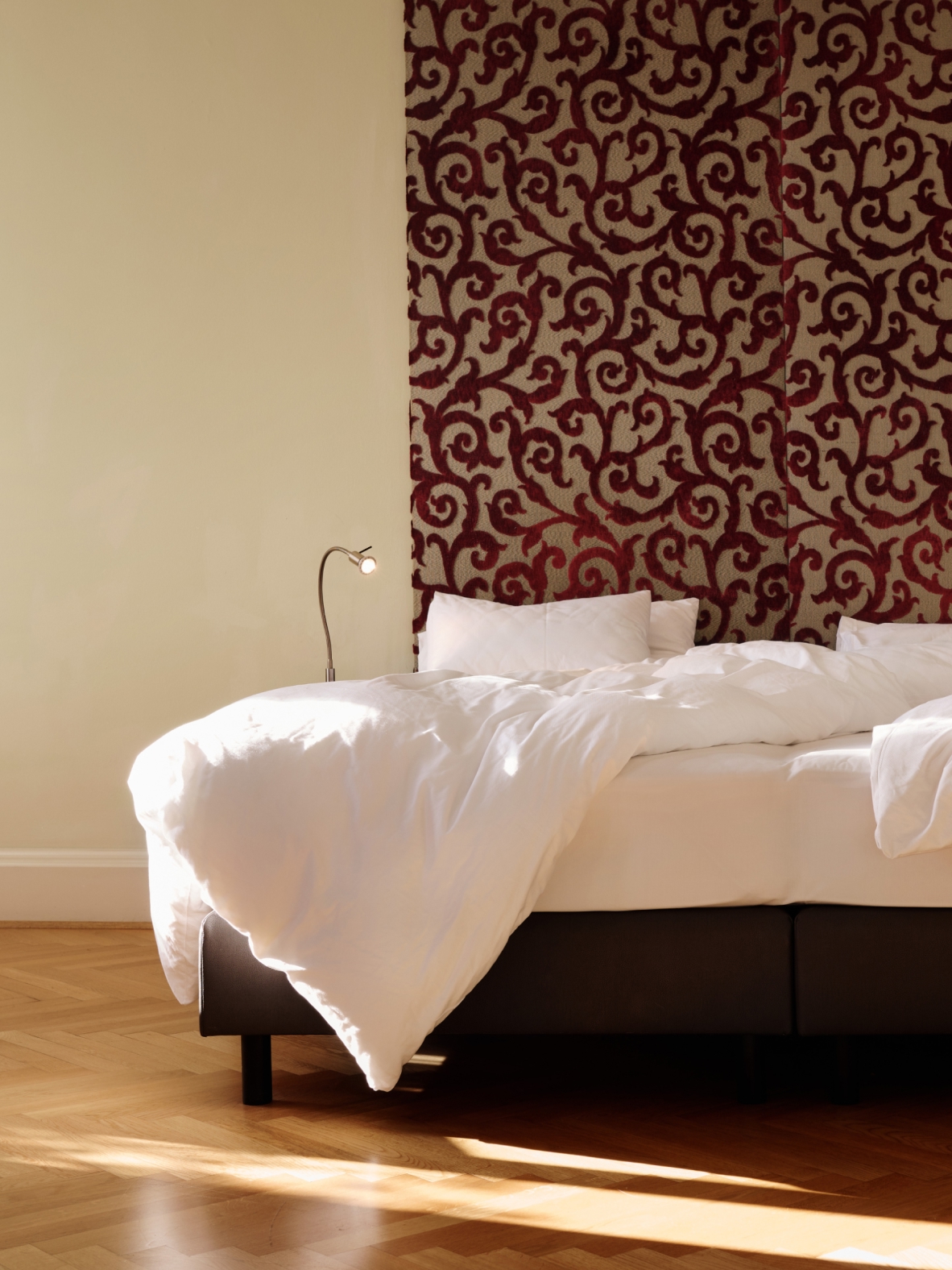 Ein Bett mit weißer Bettwäsche steht in einem Zimmer mit burgunderfarbenem und beigem Wirbelmuster an der Wand dahinter.