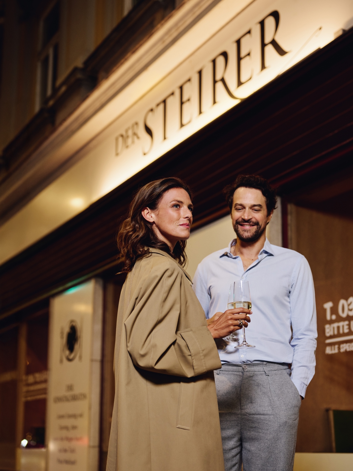 Ein Paar steht vor dem Restaurant "Der Steirer" mit Weingläsern in der Hand.