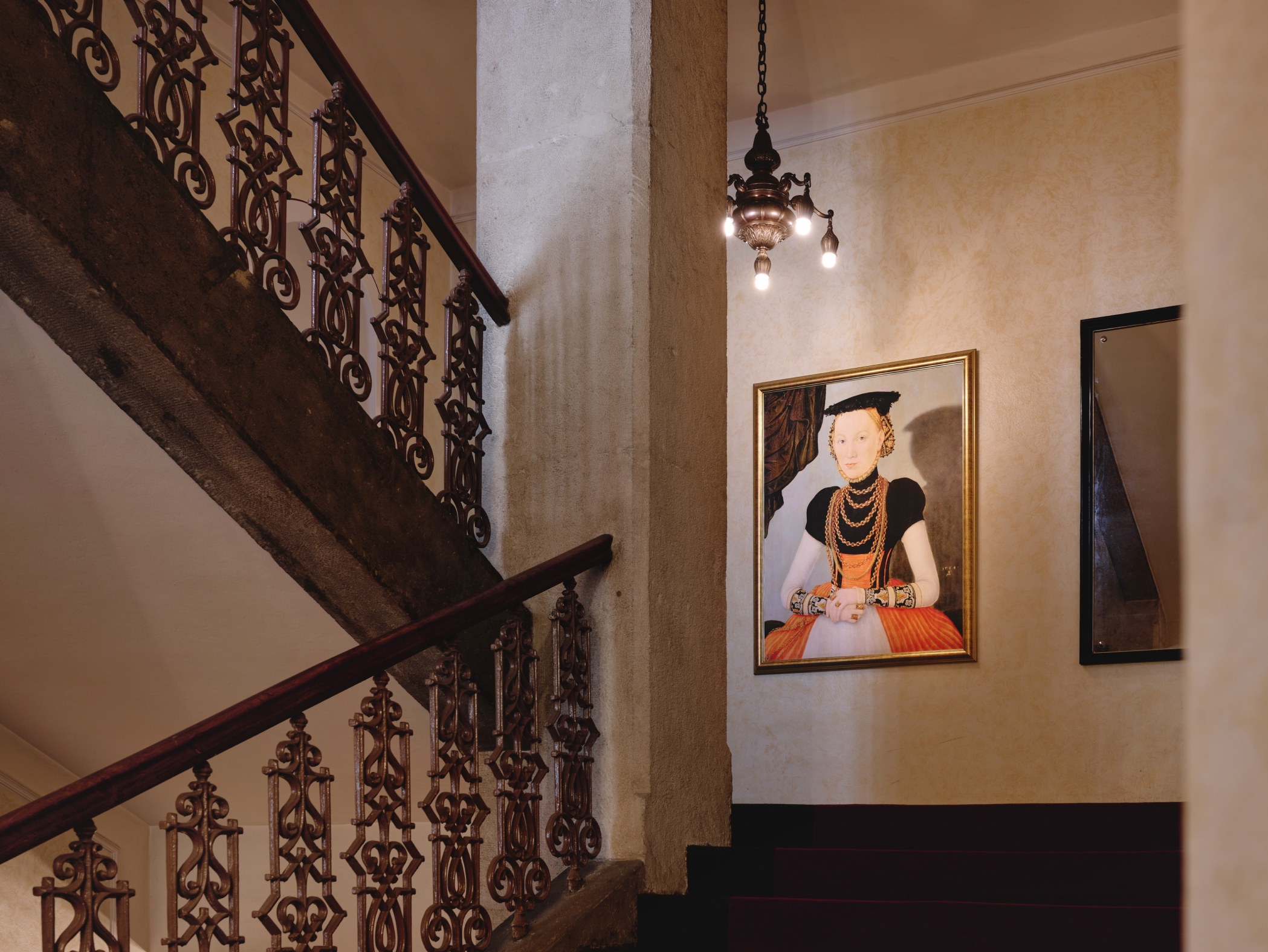 Treppe mit verziertem Geländer, Gemälde einer Frau und einer Leuchte an der Wand.