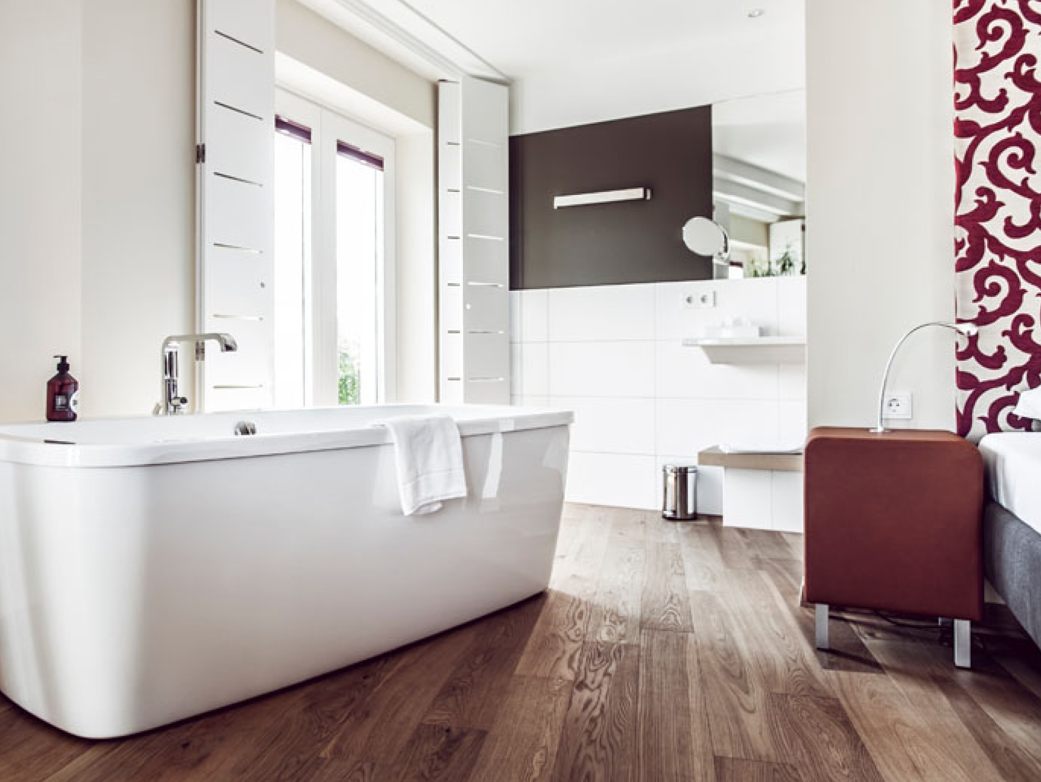 Ein Badezimmer mit einer freistehenden Badewanne, Holzböden und burgunderroten Akzenten.