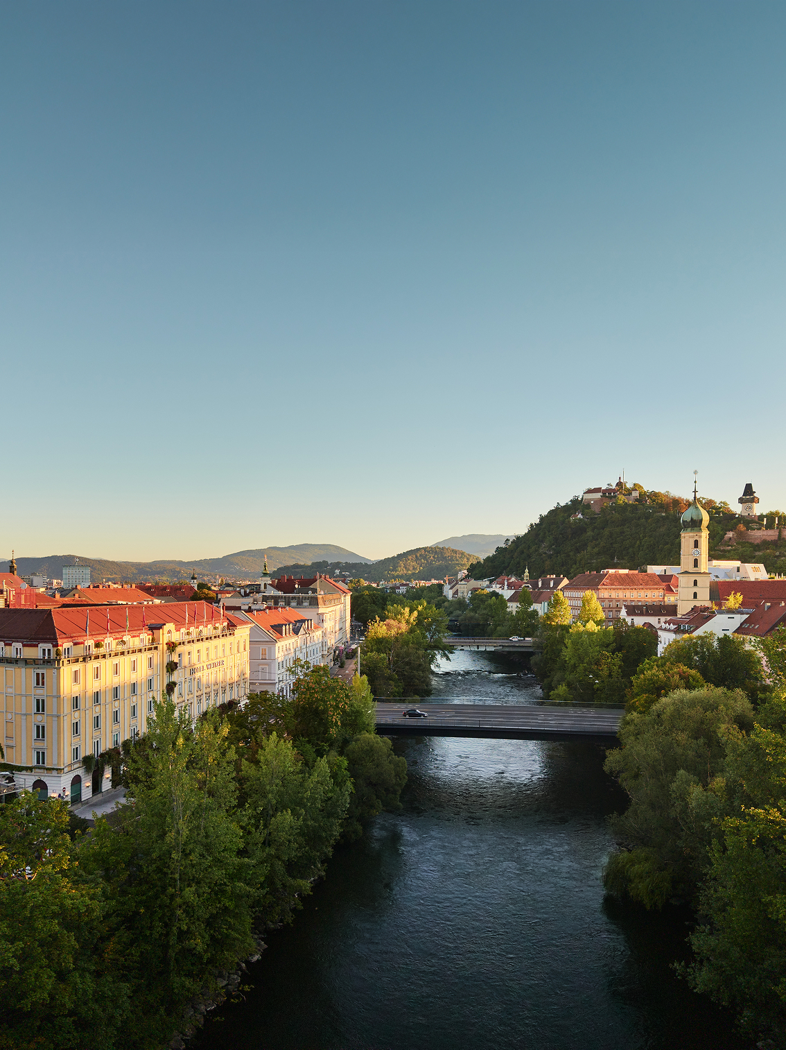 Eine Panoramaaufnahme von Graz, mit Blick auf Mur, Hotel Weitzer und dem Grazer Schlossberg